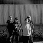 four dudes standing in front of a fence