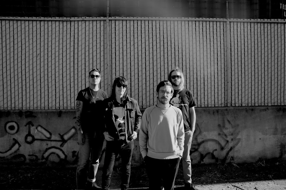 four dudes standing in front of a fence